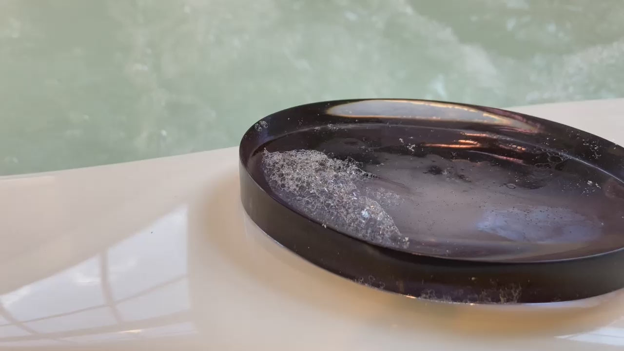 Video shows a black modern oval shaped soap dish on the edge of a jacuzzi tub