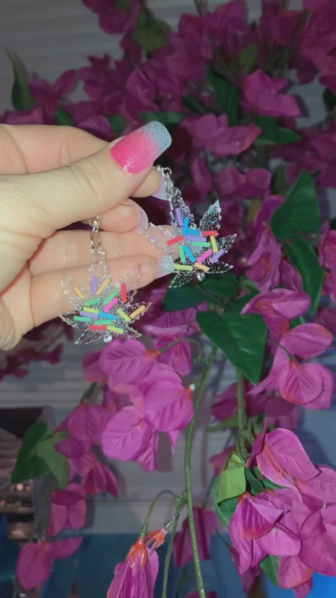 Video shows a hand holding marijuana leaf design dangle earrings with sprinkles in them 