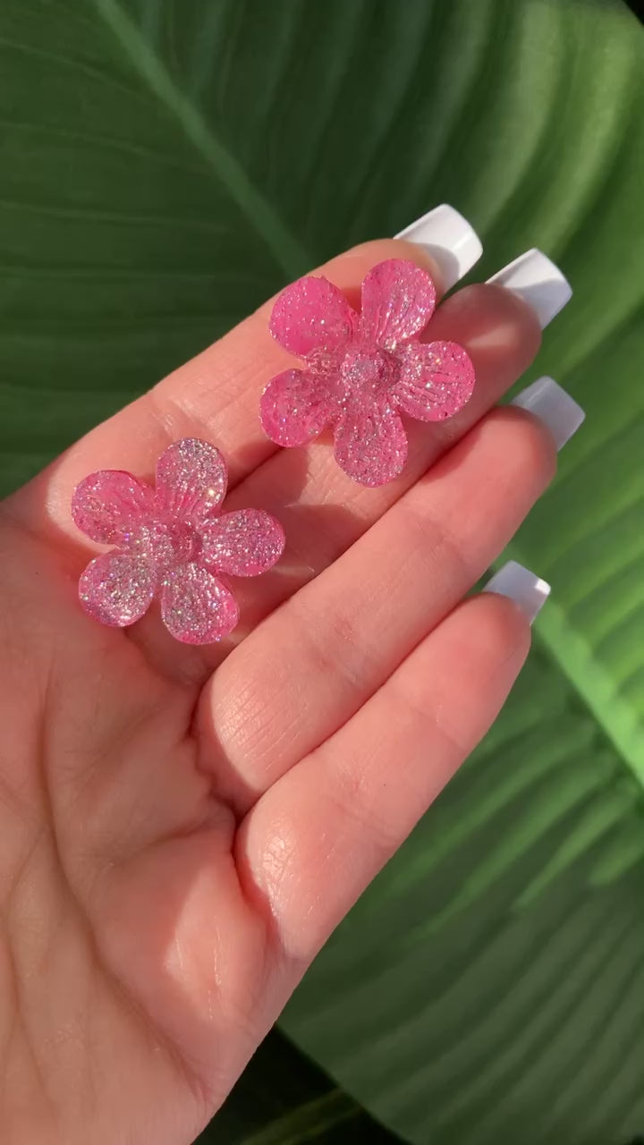 Video shows a pair of pink sparkle flower earrings in a hand 