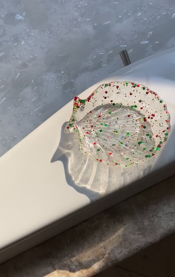Video shows a red and green sequin seashell resin soap dish on the edge of a bath tub 
