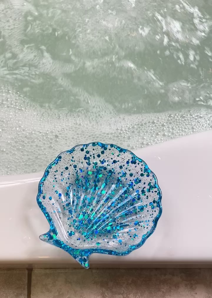 Video shows a blue seashell soap dish on the side of a running bath tub