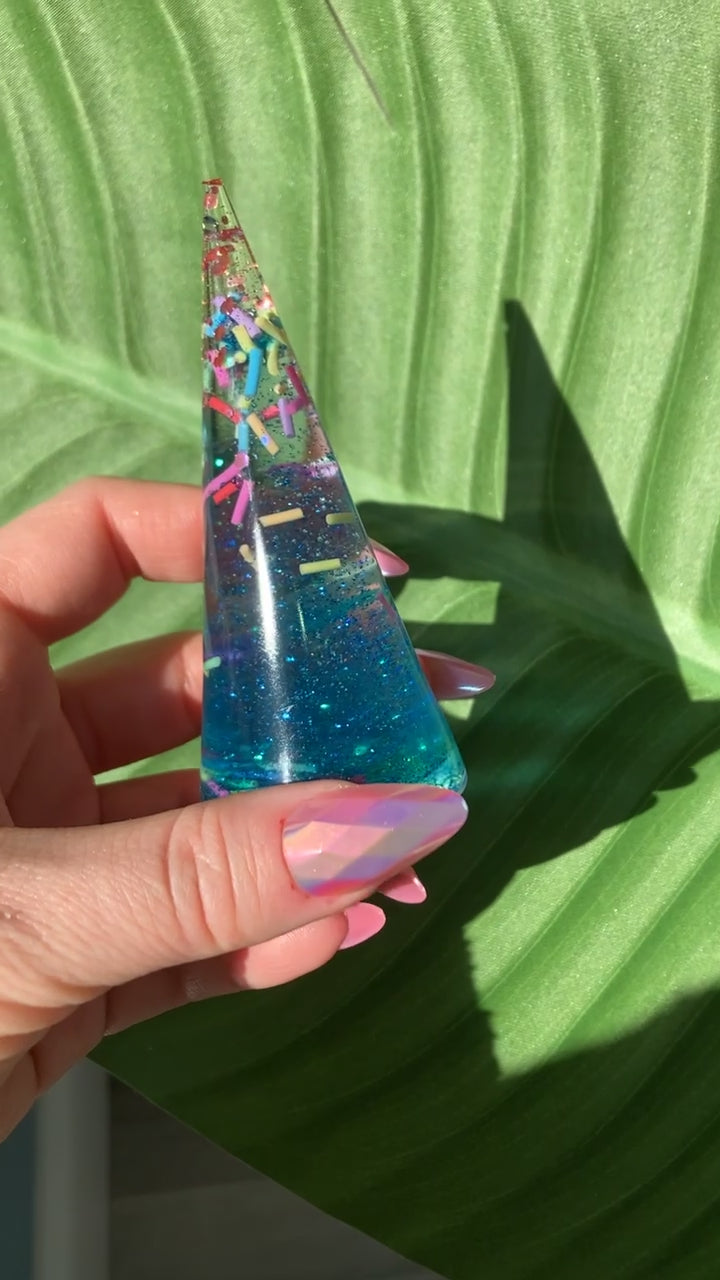 Video shows a sprinkle ring display in a manicured hand in front of a leafy background 