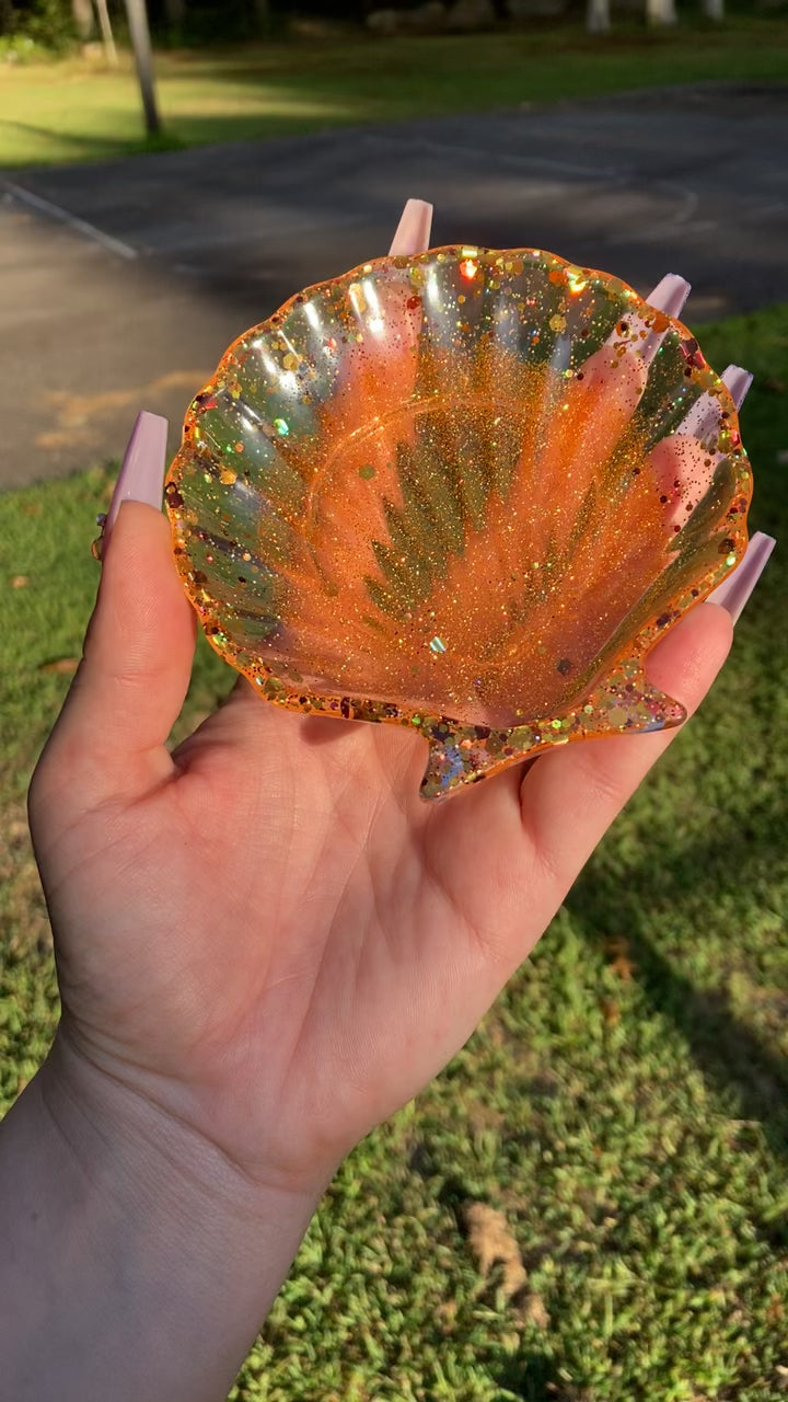 Autumn colored seashell soap dish in a manicured hand in the sun.