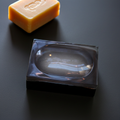 A bar of natural soap sits near a smoky resin soap dish on a dark surface.